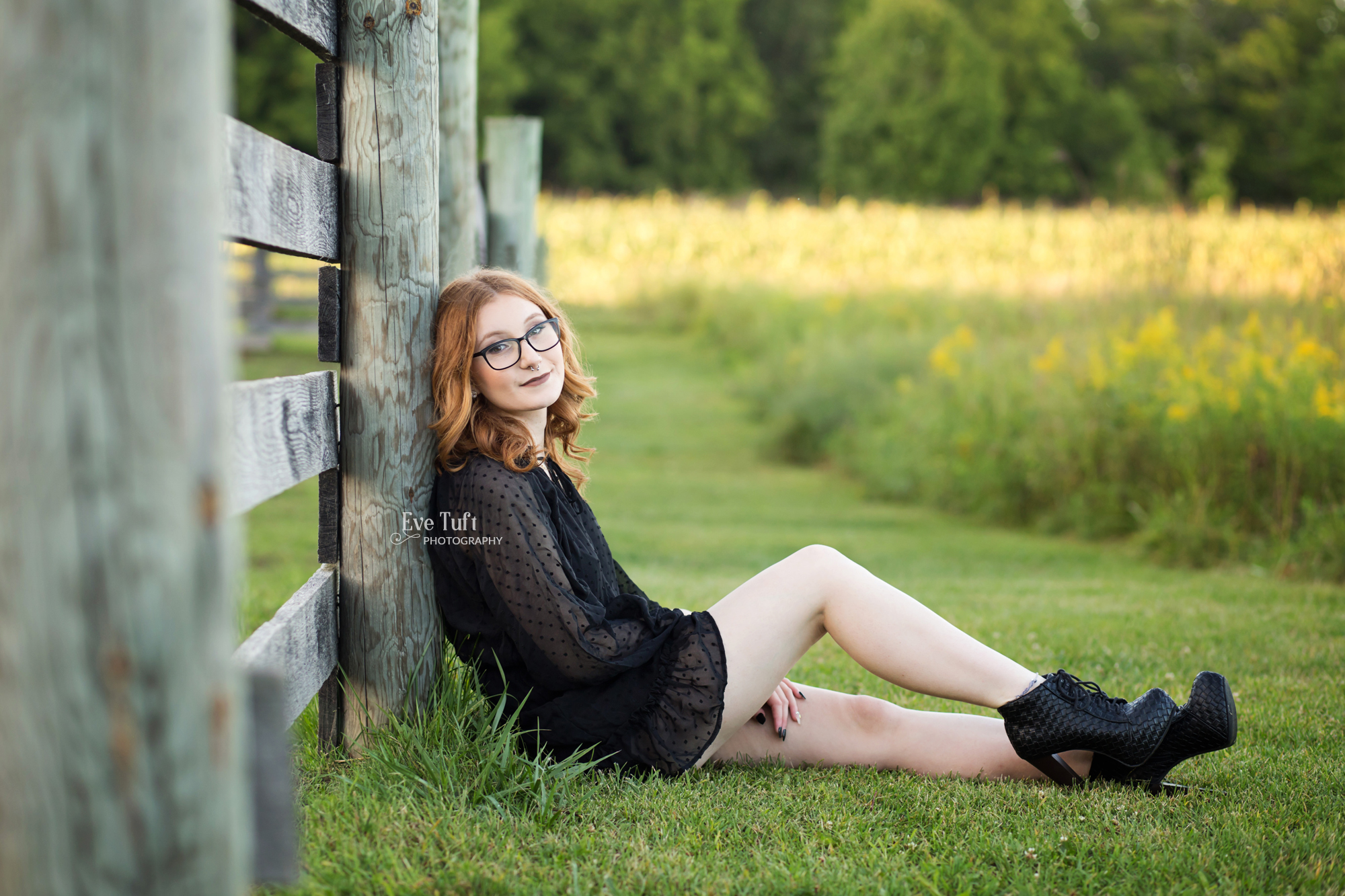 A senior girl sits against a fence at the Chippewa Nature Center in the grass | Michigan Senior Photographer