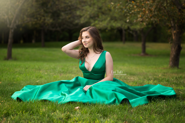 Senior girl sits in the grass while wearing a green ballgown | Midland, MI senior photographer