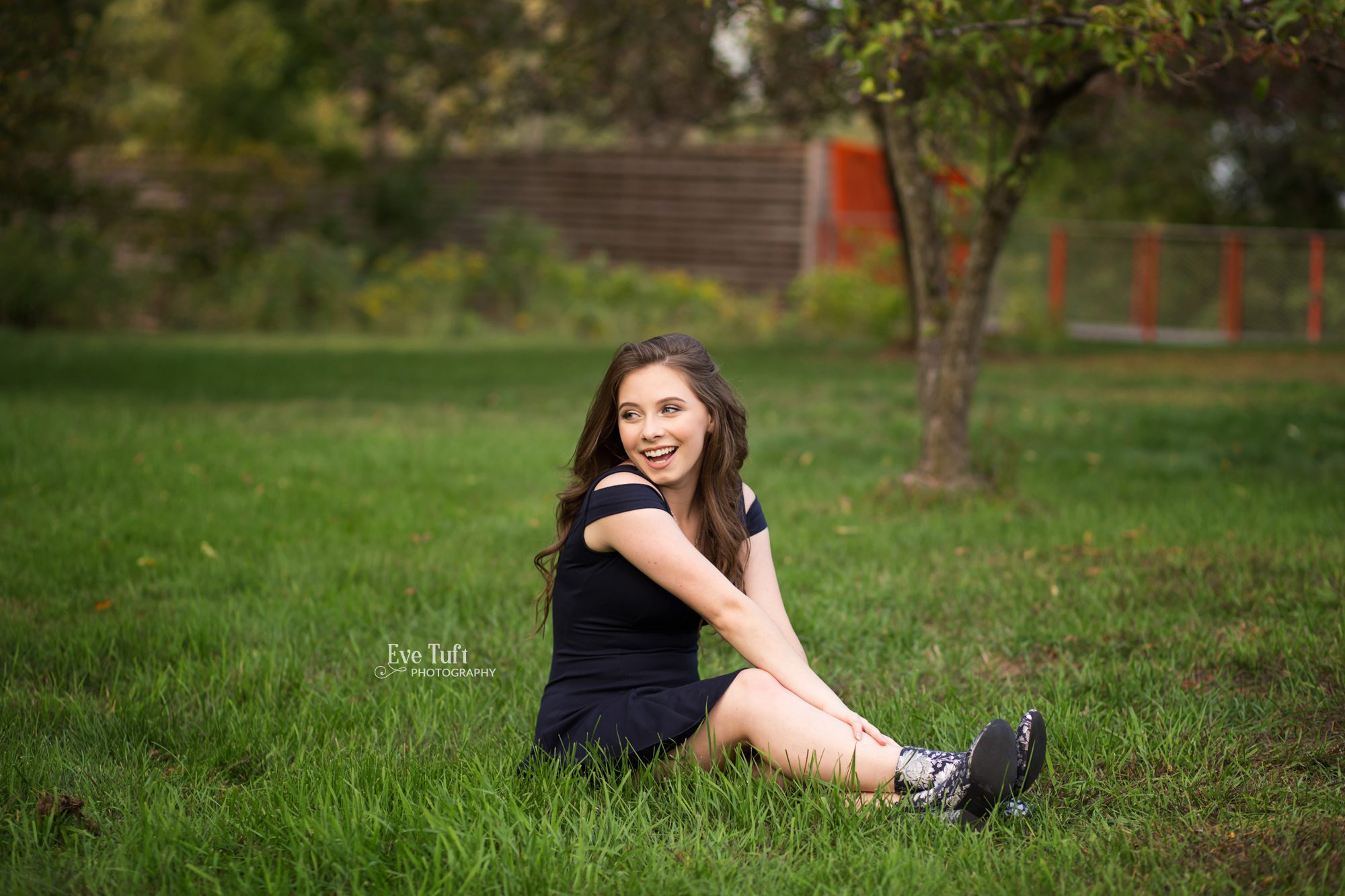 A teen girl sits in the grass and laughs at the library | Grace A Dow Senior Photographer in Midland