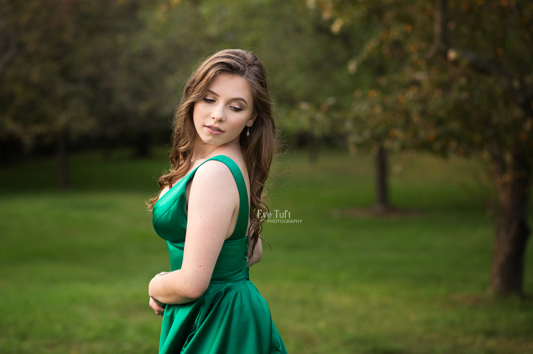 A senior glances oer her shoulder while wearing a green prom dress outside in the grass | Senior Photography in Michigan