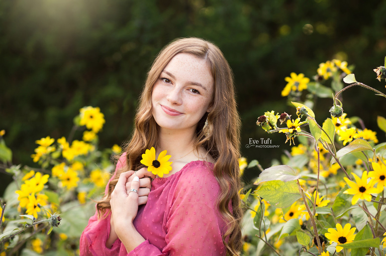 A beautiful teen holds a sunflower close as she smiles in a field of flowers | Michigan Photographer for seniors