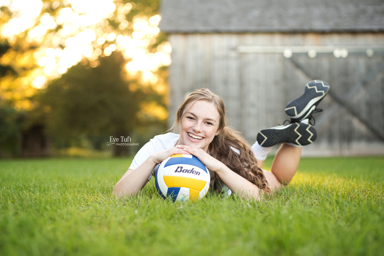 A senior girl rests her head on her ball outside in the grass | Senior Portraits in Michigan