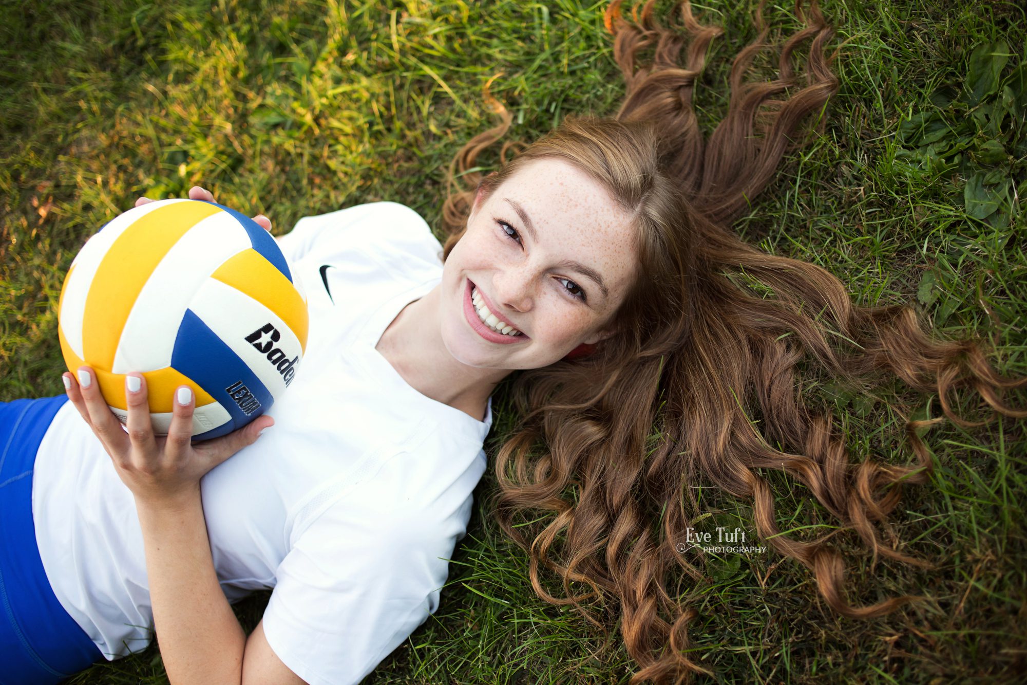 A beautiful teenage girl lies down in the grass with her volleyball at the CNC | Senior pictures in Michigan