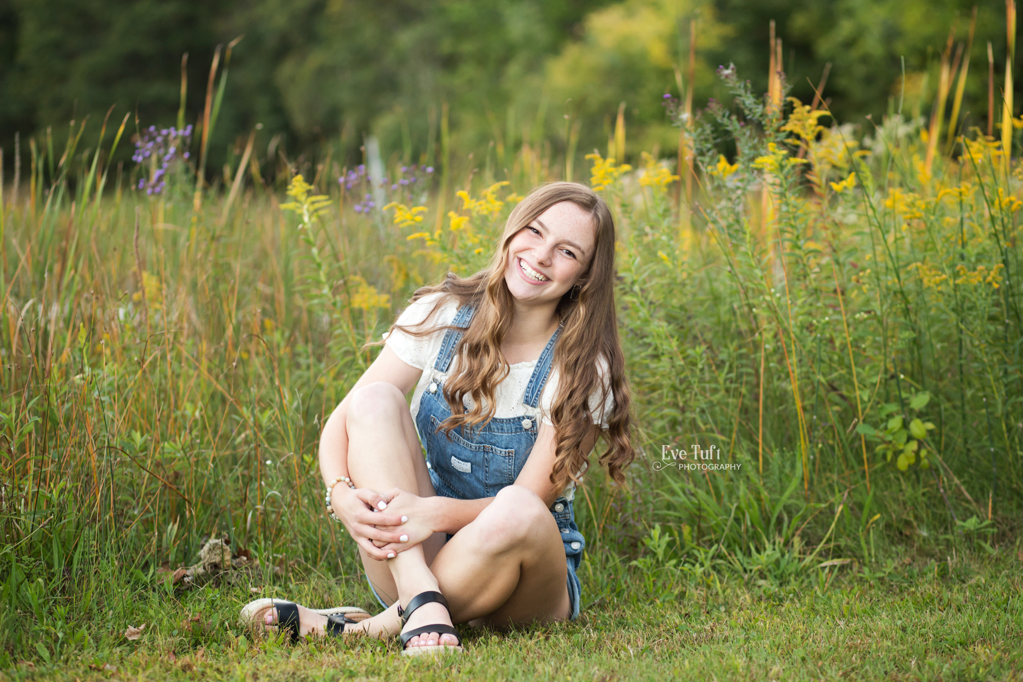 A senior girl sits in front of wildflowers at the Chippewa Nature Center | Senior Photographers in Midland, Michigan