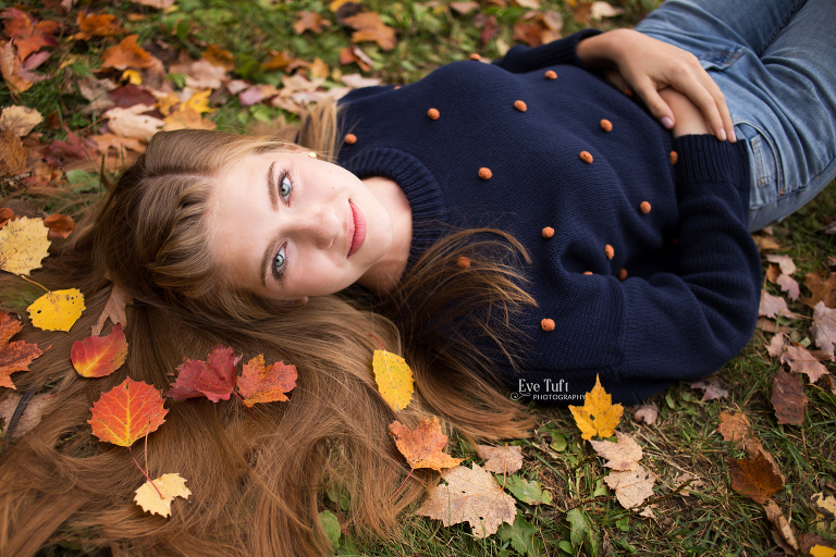 A beautiful senior girl lies down in the fallen leaves outside at City Forest | senior photographers in Midland, Michigan