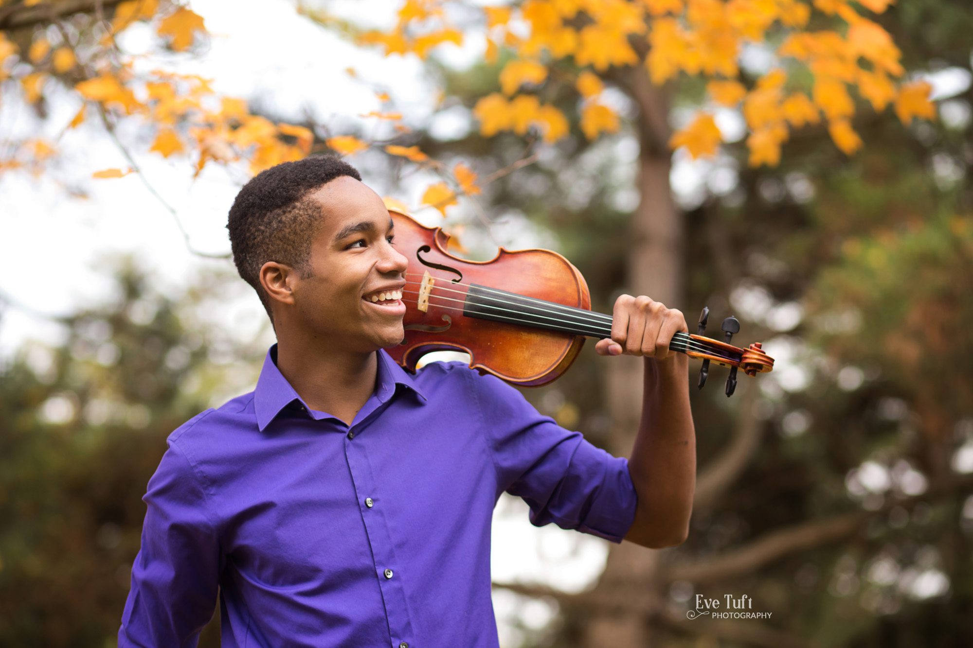 A senior boy holds his violin up on his shoulder outside in the fall at Dow Gardens | Midland, Michigan Senior Photographers