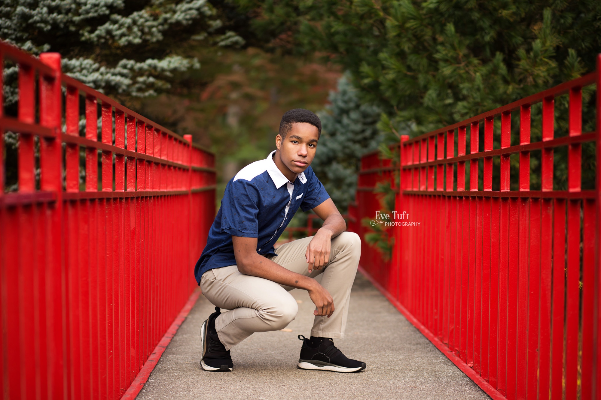 A senior guy squats on a red bridge at Dow Gardens | Michigan Senior Photographers