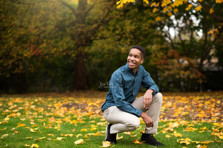 A handsome teenager squats outside in the fall for his senior session | Midland, MI senior photographers