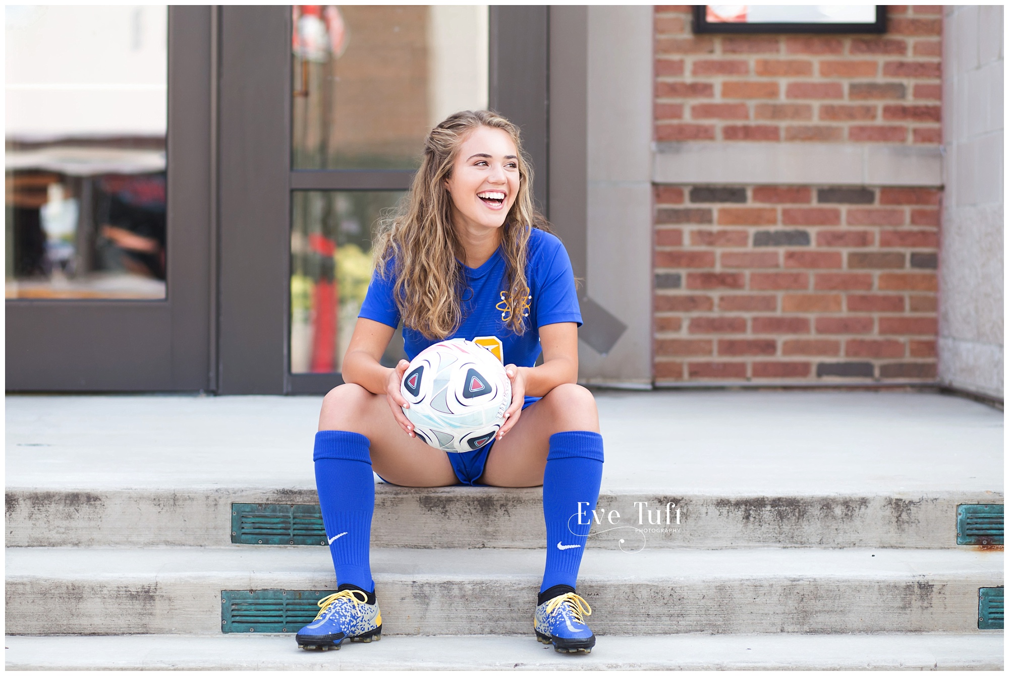 A senior girl laughs while sitting on steps with her soccer ball for her two sports session | Midland, MI senior photographer