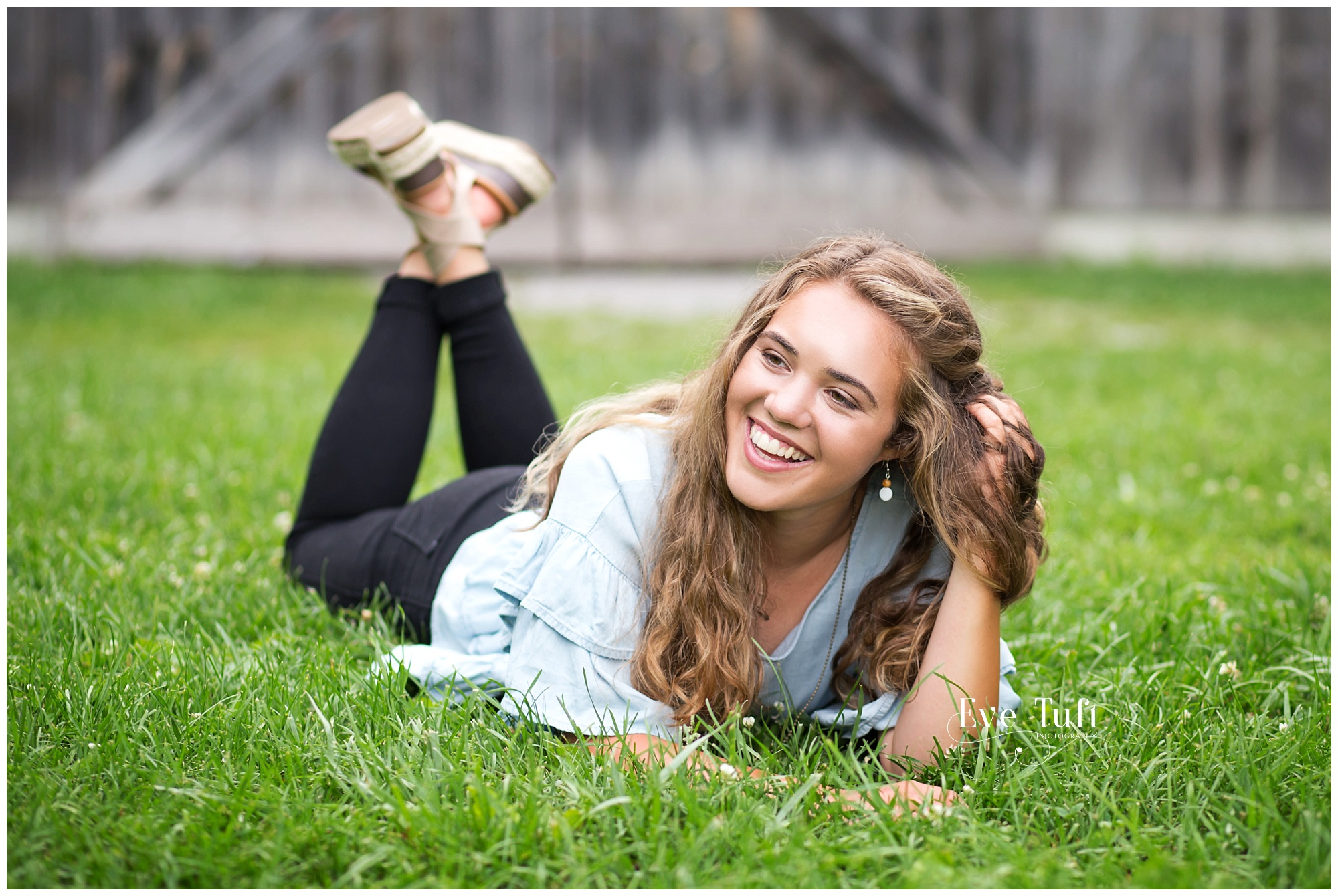 A teen lies on the grass in front of a barn and laughs | Midland, Michigan senior photographers