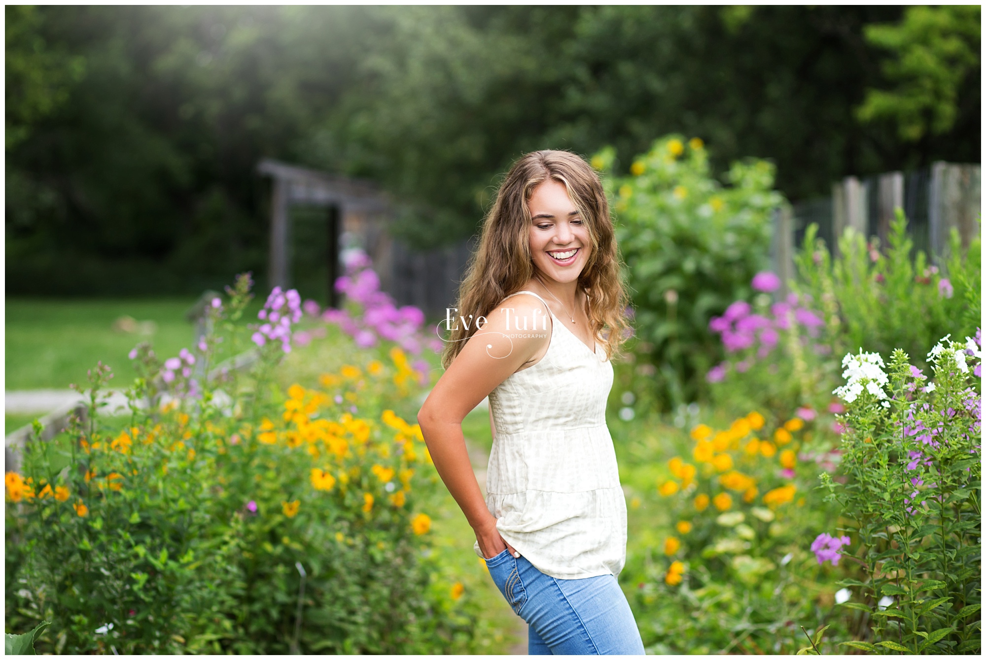 A teen stands in a garden of flowers outside for her portrait session | Senior photographer in Midland, MI