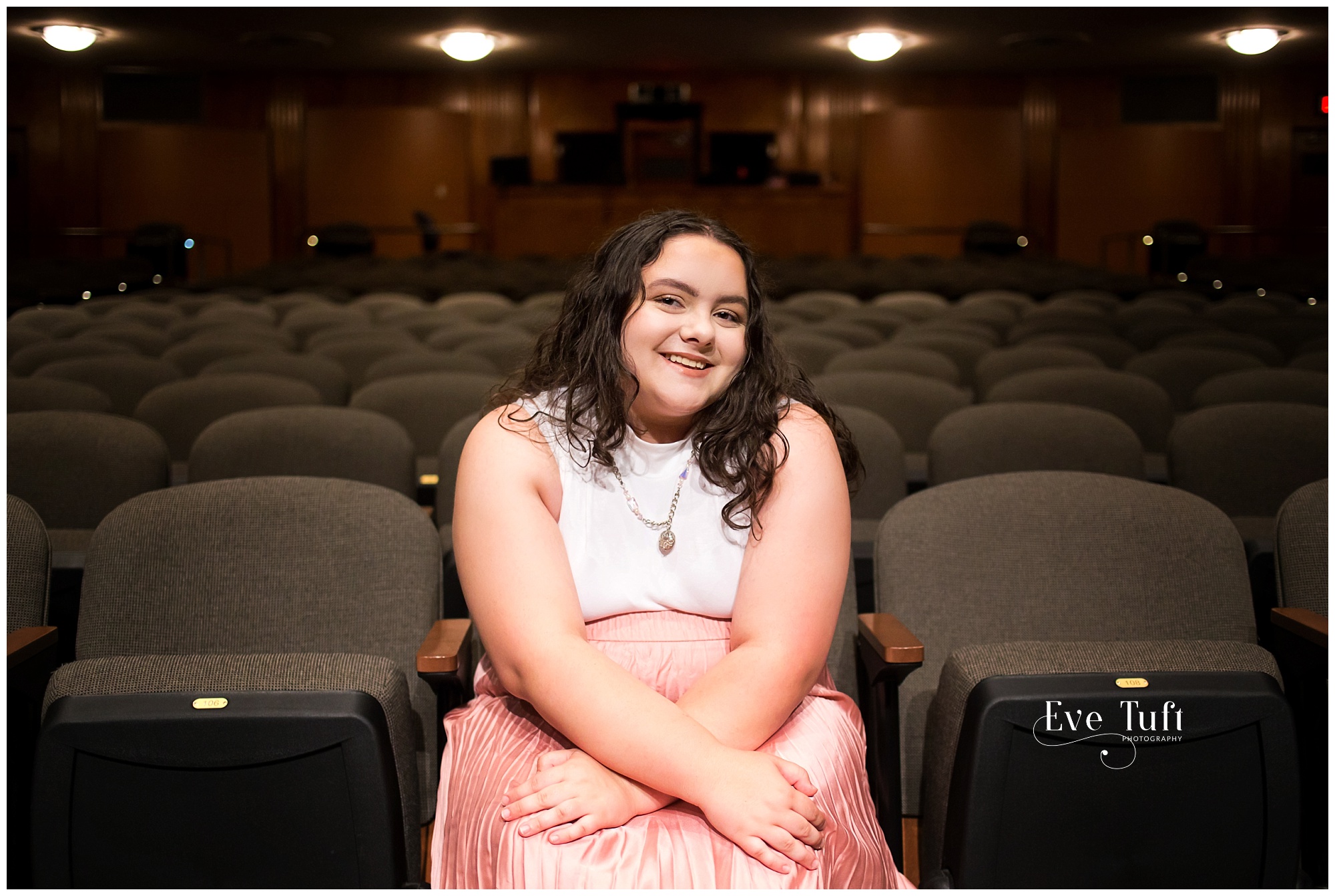 A teen sits in the audience on a chair in an auditorium in a theater | Senior Photographers in Midland, MI