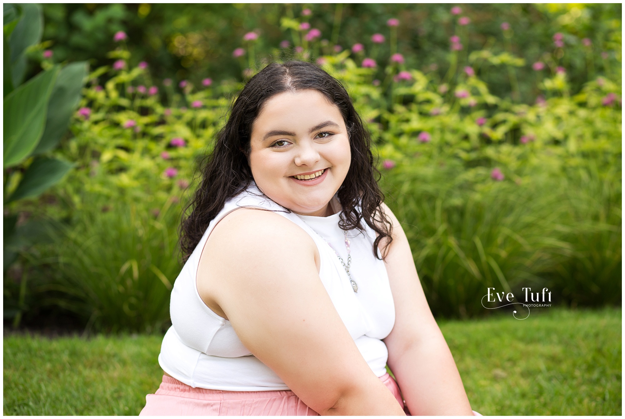 A senior girl sits on the grass in front of flowers at Dow Gardens | Senior Photorapher in Midland, Michigan