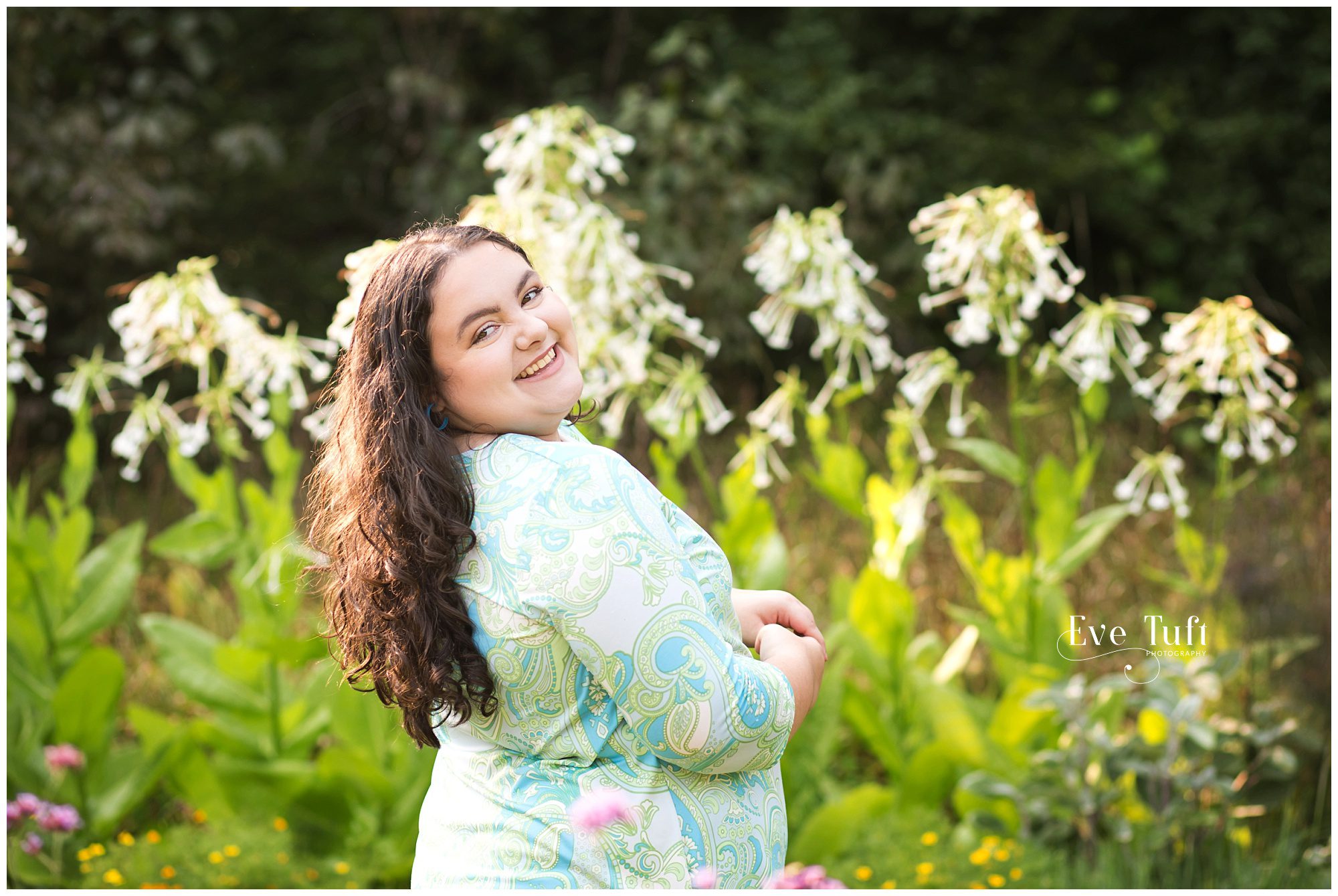 A teenager looks over her shoulder near flowers outside | Senior Sessions in Midland, MI