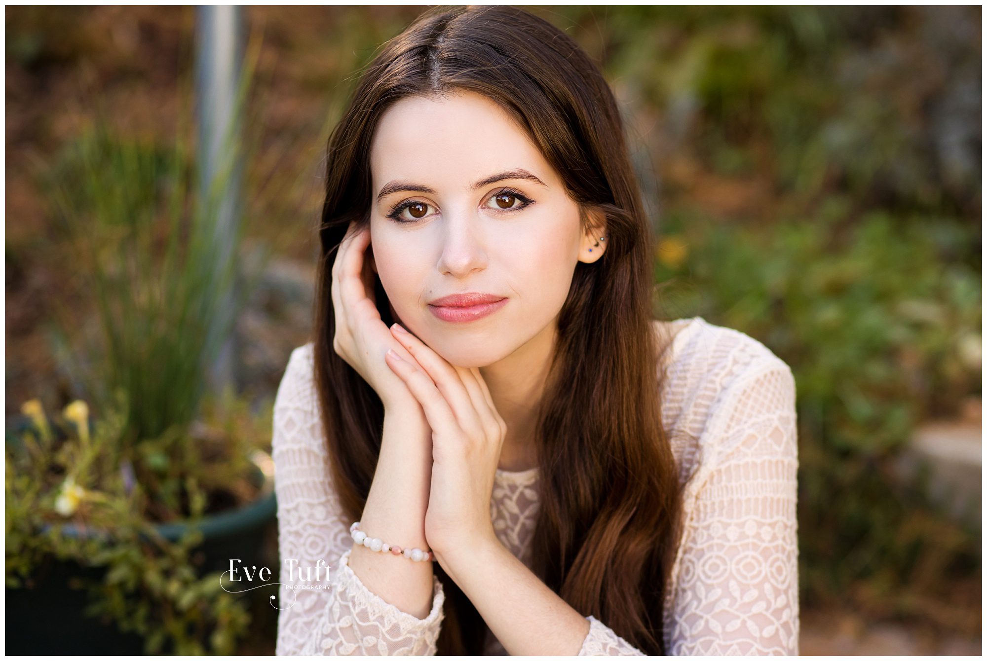 A beautiful teenager puts her hands up near her face outside in a garden | Senior Portraits in Midland, MI