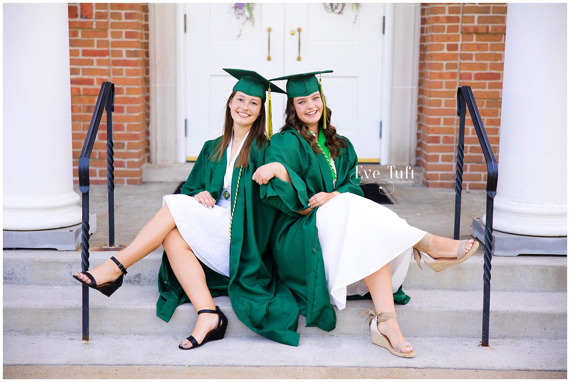 Two senior girls sit back-to-back outside in their caps and gowns | Midland, Michigan Senior Photographers